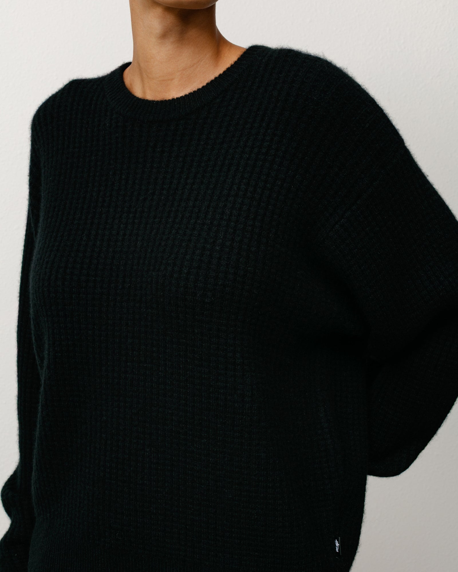 Person wearing a black sweater against a neutral background