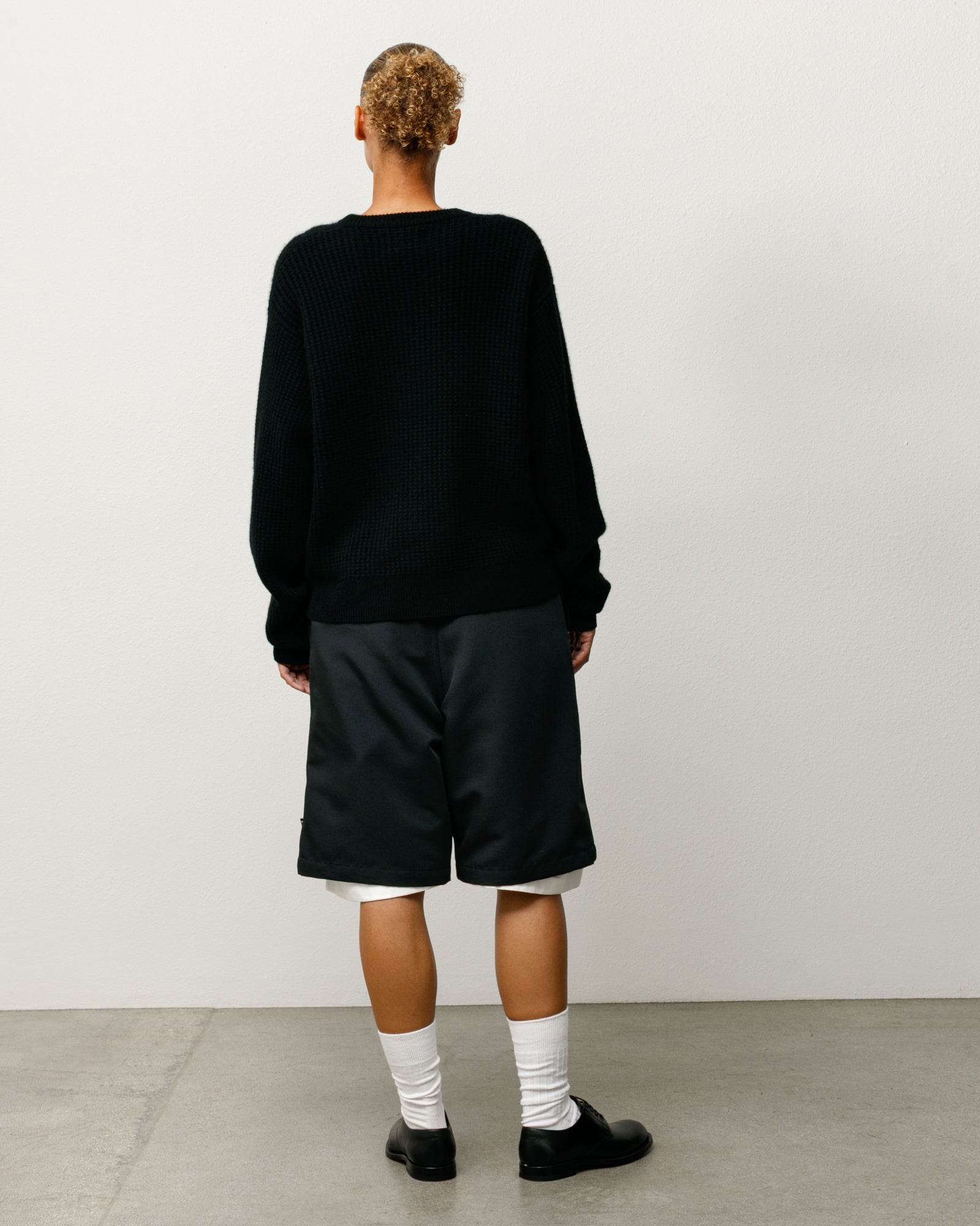 Person wearing a black long-sleeve shirt and black shorts against a white background