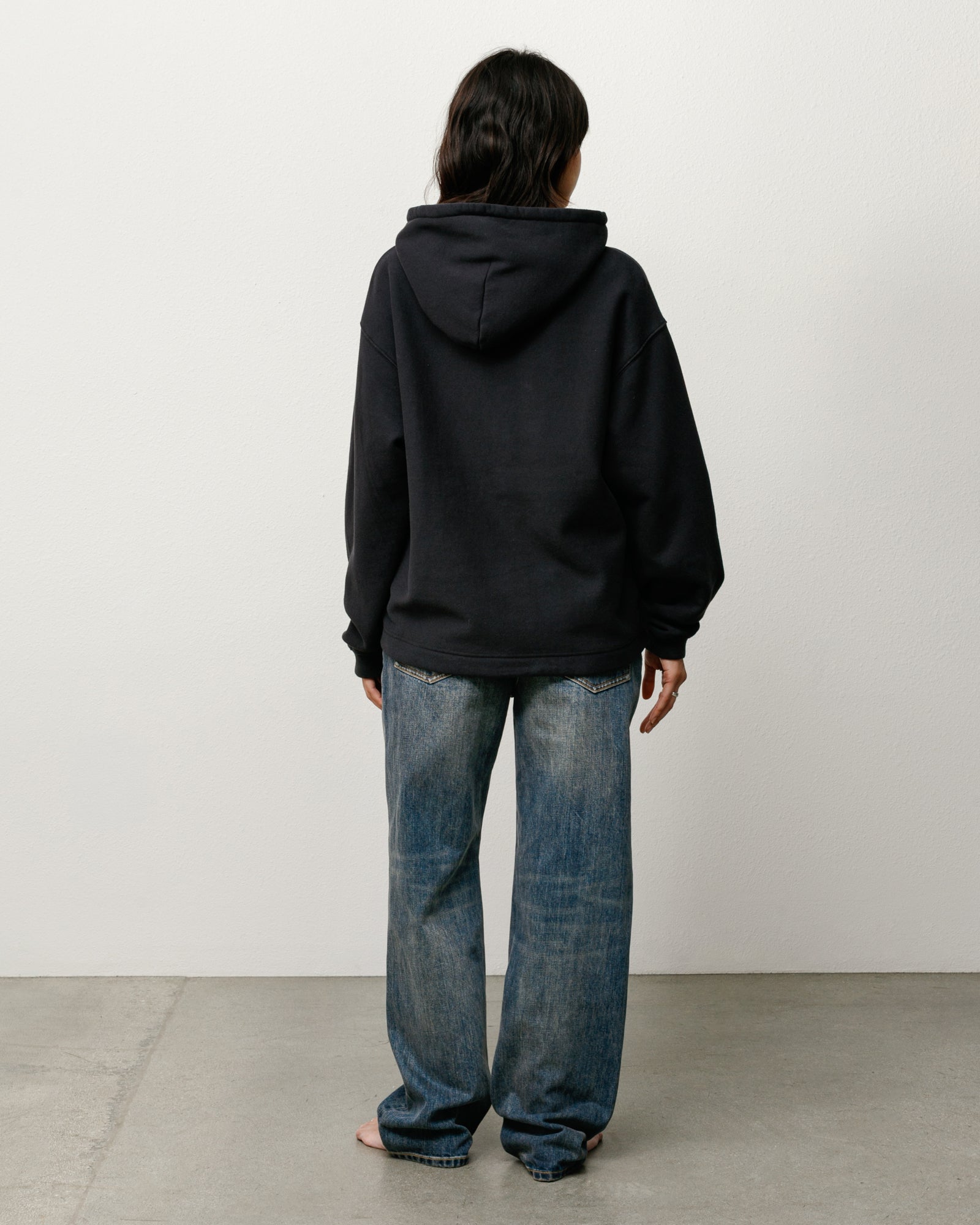 Oval Pullover Hoodie in Black, unisex; back view on model with relaxed fit and roomy hood.