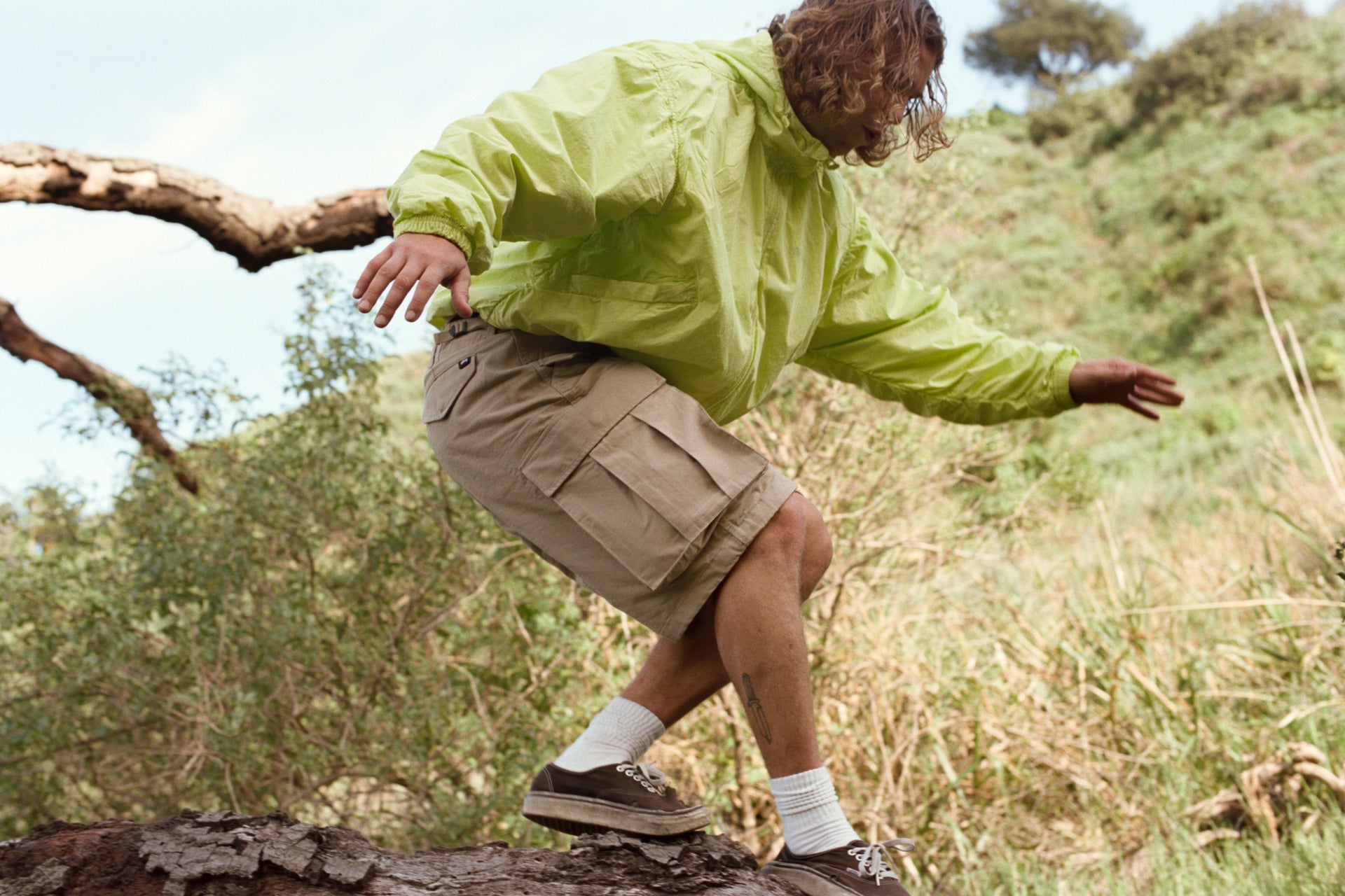 Person in a Double Cotton Hooded Jacket in Lime and Cargo Short Ripstop in Khaki balancing on a log in a natural setting.