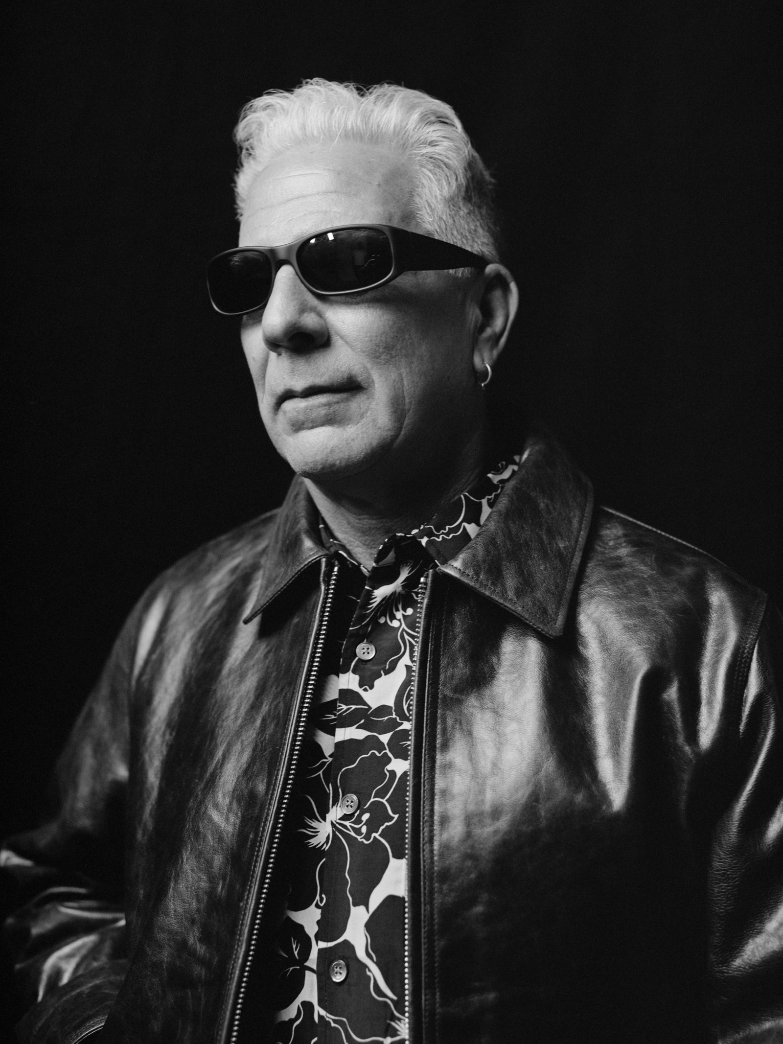 Person wearing sunglasses, a Garage Leather Jacket, and a floral Hawaiian shirt against a black background.